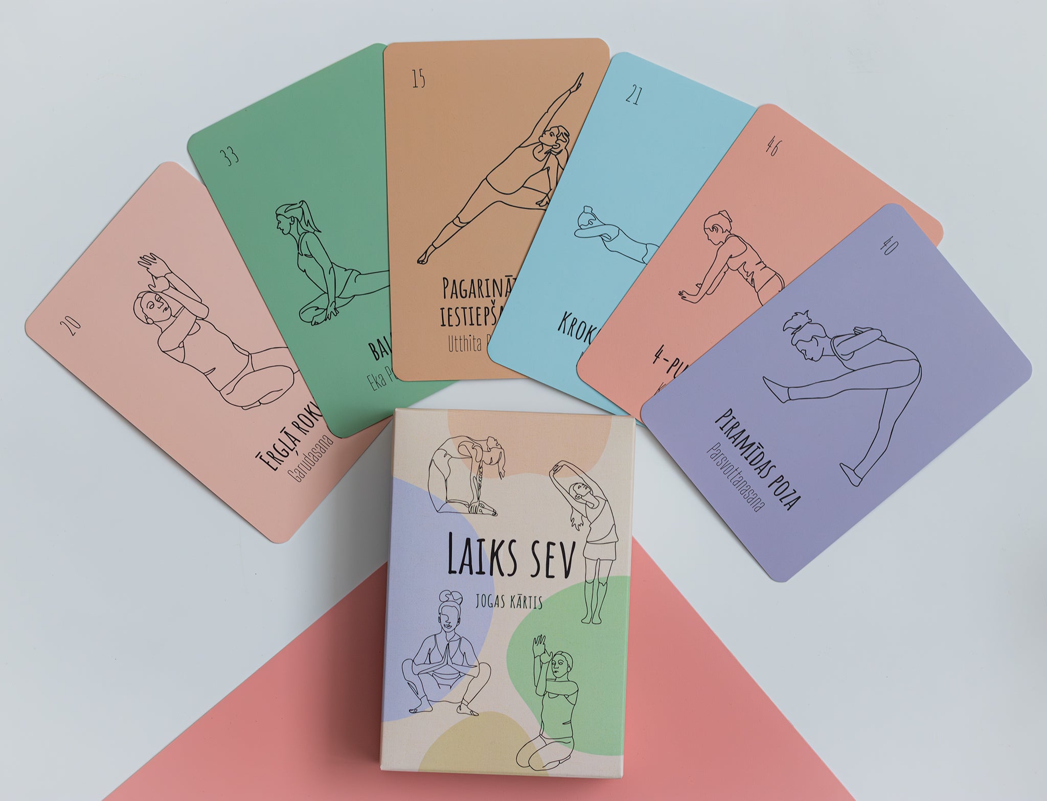 A set of yoga cards titled 'LAIKS SEV YOGA CARDS' arranged on a white background with pink and green paper accents. The cards are fanned out behind the box, showing different yoga pose illustrations in black line art on pastel-colored card backs.